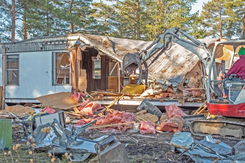 A mobile home being demolished by an excavator