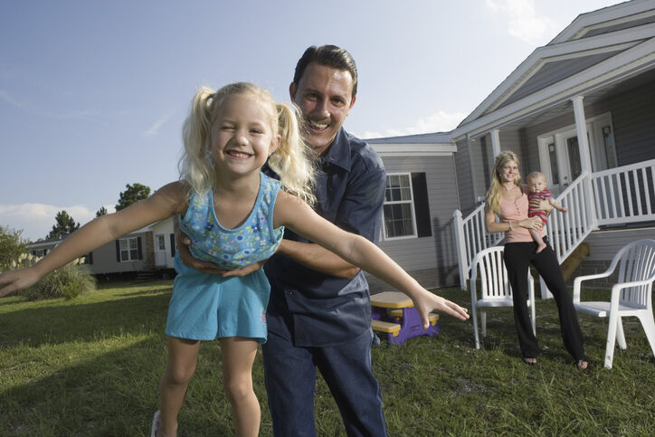 Portrait of a man playing with his blue-collar family in front of a trailer home